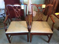 Front view of the two wooden dining arm chairs showing carved backs and beige bee print fabric seats.