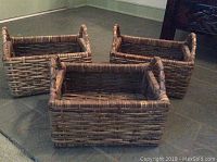 Three rectangular woven baskets with tall handles on short sides, displayed on floor.