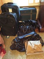 Photo showing two black Concourse suitcases (one carry-on and one larger checked), a black shiny duffle bag, two tote bags on floor, and vintage green American Tourister suitcase behind near window.