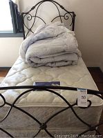 Twin iron bed frame with white quilted mattress and folded bedding on top.