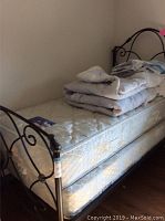 Black iron twin bed frame with scrollwork, Serta twin mattress and box spring underneath, visible corner of mattress and frame.