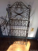 Rectangular metal wire plant stand with three shelves, showing decorative scrollwork and structure