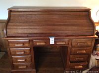 Front view of the solid oak roll top desk with the roll top closed, showing six small drawers, one file drawer, and a center drawer.