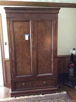 Front view of tall wood entertainment armoire with paneled double doors and a large lower drawer.