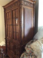 Front side view of tropical-style wooden armoire showcasing carved details and rattan panels on doors and sides