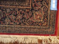 Close-up of the rug edge showing ivory fringe and detailed border pattern in burgundy, navy and gold colors.