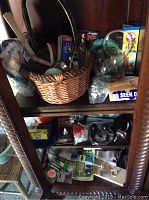 Shelf holding a woven basket with paint brushes, yarn balls, rust neutralizer spray can, and other small hardware items including a round magnifying glass and glass globe.