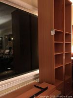 Side view of one tall brown wooden IKEA bookcase showing multiple shelves and two lower drawers stacked side-by-side in a room with large window and visible furniture reflection