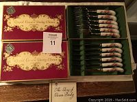 Two original red and gold Royal Crown Derby China boxes, each containing cutlery with porcelain floral handles inside green felt lining.