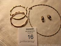 Overview of three hollow two-tone gold bangles, two-tone gold huggie hoop earrings, and three-tone gold necklace laid flat.