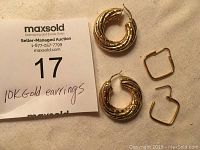 Photo showing the large hollow round 10K gold hoops and square-shaped hoops against a light fabric background with auction label.