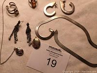 Silver and amber jewelry items including ring, earrings, lockets, and necklace on a beige background with auction card.