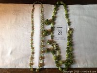 Photo displaying two vintage green bead and crystal necklaces alongside matching clip-on earrings, showing colors, bead types, and overall condition.