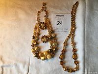 Two vintage gold tone bead and crystal necklaces and a pair of clip-on earrings arranged on a tan fabric background.