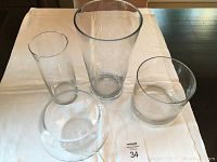 Four clear glass vases displayed on a white cloth, varying in height and shape, showing the entire set from the top view.
