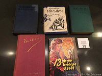 Five vintage hardcover books arranged on a dark surface, showing covers including 'I'm Alone', 'Goodbye Mr. Chips', 'Blaze's Beauty', '13 Three Bridges Street' and one book spine only.