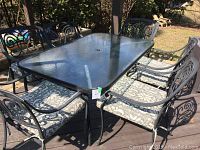 Full view of rectangular glass-top table and six matching metal chairs with cushions on deck