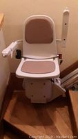 Front view of Acorn stairlift chair showing beige padded seat and armrests mounted at base of stairs