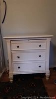 Front view of the white dresser showing the three drawers and metal knobs with decorative molding.