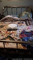 Full view of queen size brass bed made of polished metal with headboard and footboard, showing the bed frame standing with a quilt and pillows on mattress.