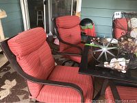 Set of two red striped cushioned patio chairs with dark metal swivel rocking bases and armrests placed around a black glass outdoor table as seen from the front at an angle