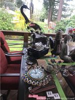 View of the large black and yellow metal peacock wind chime on a patio table surrounded by other decorative items including a peacock clock and yard art.