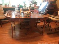 Wide shot of the oak pedestal dining table with various items on top, shows two leaves extended and folding legs beneath for balance.