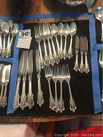 Full layout of flatware pieces—knives, forks, spoons—on black cloth with blue tape borders