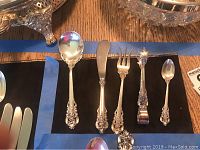 Photo of Wallace sterling silver serving pieces including spoon, spreader, fish fork, tongs, and small spoon all in Grand Baroque pattern