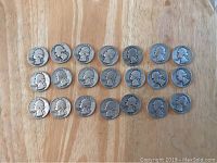 Front view of 21 USA silver quarters arranged in rows on a wooden surface, showing wear and various mint marks.