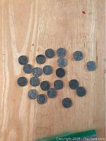 21 steel pennies scattered on a wooden surface showing their obverse face with Lincoln's profile.