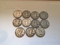 Eleven Franklin silver half dollar coins arranged on a white surface showing front profiles of Benjamin Franklin.