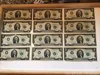 Twelve US two-dollar bills arranged in a tray showing front sides, all featuring Thomas Jefferson and distinct serial numbers.