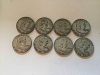 Top view of obverse side of eight silver half dollar coins showing dates and 'In God We Trust' text.