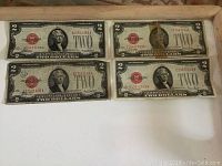 Four United States Two Dollar bills with red seals laid out in a wooden tray. All bills show signs of wear and use.