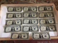 Display of all fourteen 1 dollar silver certificate bills laid out in a tray, arranged in rows showing their fronts.
