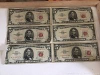 Photo of six US five dollar bills arranged in two rows of three, showing front sides with red seals and Abraham Lincoln's portrait.
