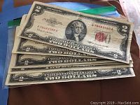 Front view of six US $2 bills showing red seals and serial numbers