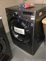 Front view of stainless steel washer showing LG True Steam branding, control panel, circular front door with 'dejar la puerta abierta por favor' sign and #877 sticker