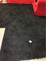 Photo showing the texture and color of the large dark shaggy rug laid out flat on the floor with red furniture around it.