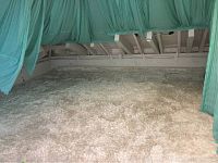 Photo showing large light-colored shag area rug covering a floor under a ceiling with exposed wooden beams and green curtains.