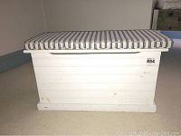Front view of solid white wooden chest with blue and cream striped cushion on top.