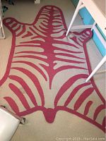 Full view of pink zebra striped rug on carpeted floor with table legs visible.
