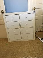 Front view of white 8-drawer Ikea storage cabinet with silver knobs, visible minor scuffs and scratches.
