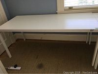 Image showing full length of large white rectangular desk/table with metal legs on carpeted floor near window