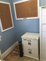 Photo of corner with the two cork boards mounted on the wall above the file cabinet and Vornado space heater on the floor next to it.