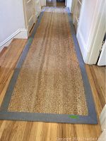 Full length view of the sisal runner rug laid out in a hallway on a wooden floor, showing the natural fiber surface and gray fabric border.