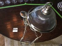 Chandelier with ribbed glass dome shade, polished metal fixture, and attached chain lying on table.