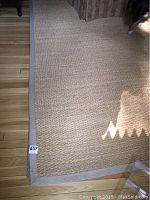 Close-up of one corner showing woven sea grass texture and jute trim on wooden floor.