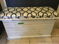 Front view of the white wooden chest with patterned cushion on top showing stains and hinge area.